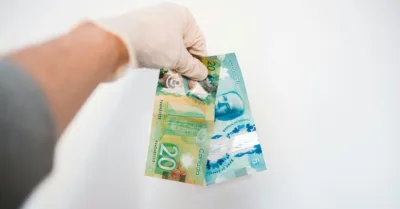 Gloved hand holding Canadian money in front of white background
